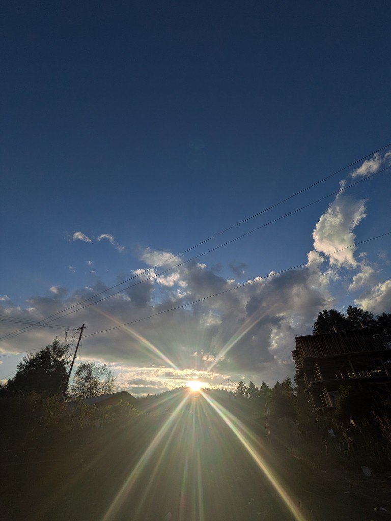 The sun bursting through cloud at the end of the day, a wooden house on the right