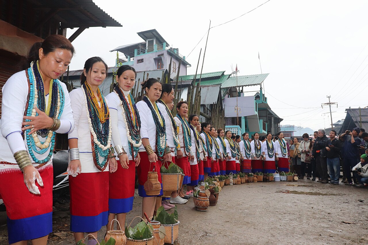 Apatani women in white blouses, red skirts, and many strands of beads, standing in a line with cane baskets during Myoko