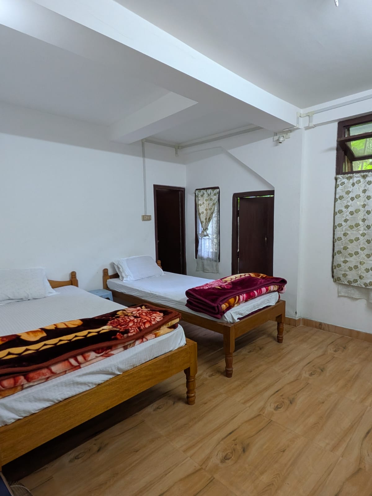 A wooden double and a wooden single in a white room, with floral blankets and windows onto trees