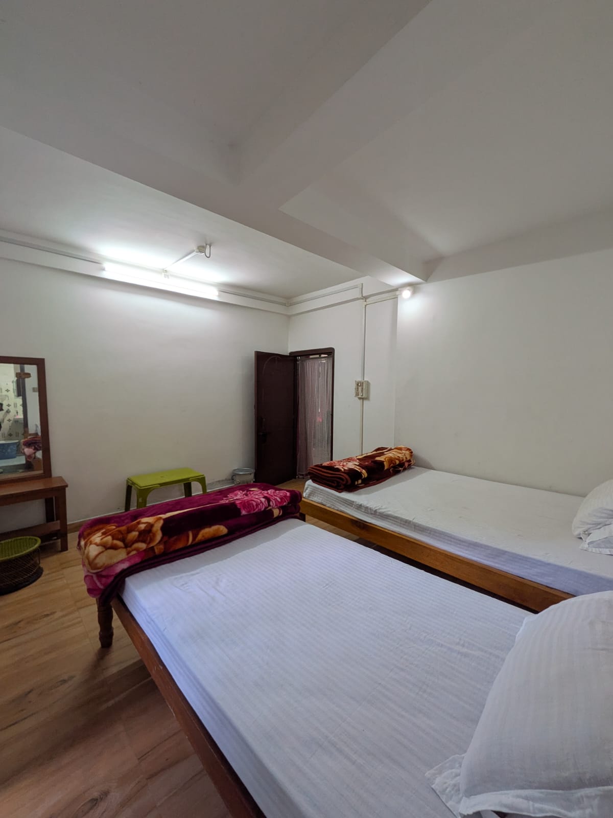 Room 1 from the foot of the beds, with a mirror, a green stool, and the door