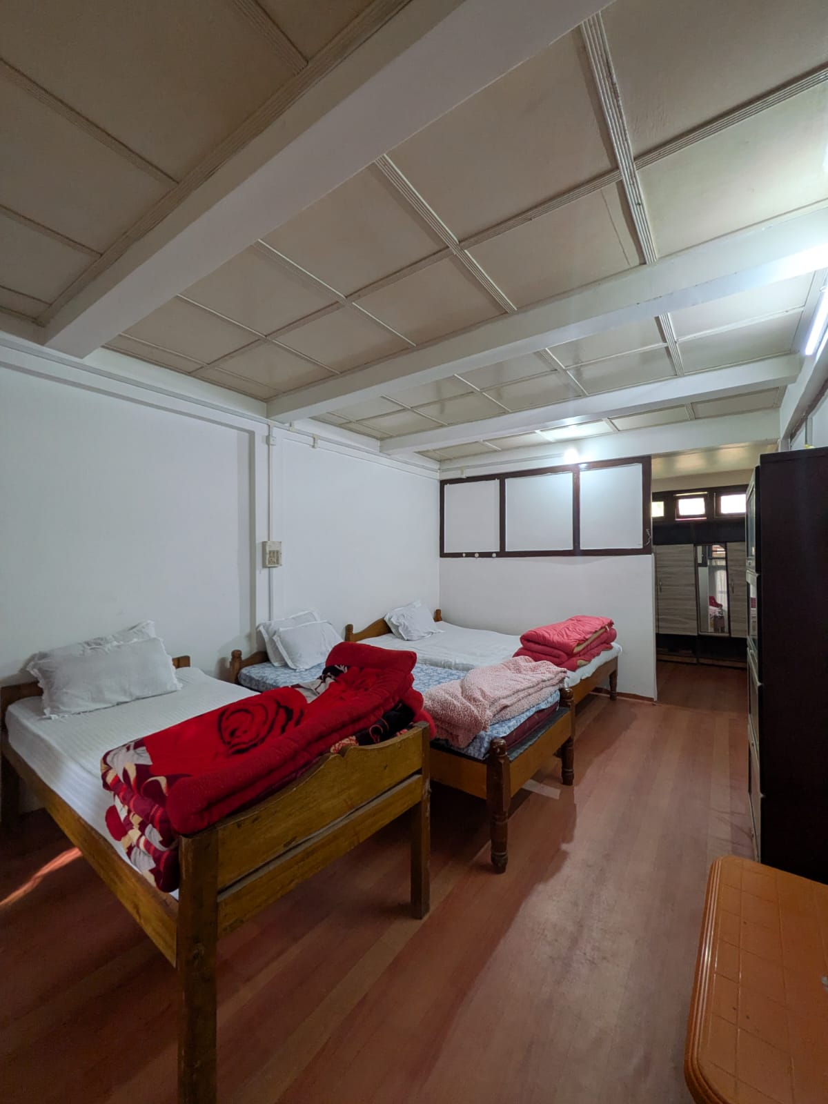 Wooden beds with red and pink blankets in a white room. One extra bed is still in the photograph