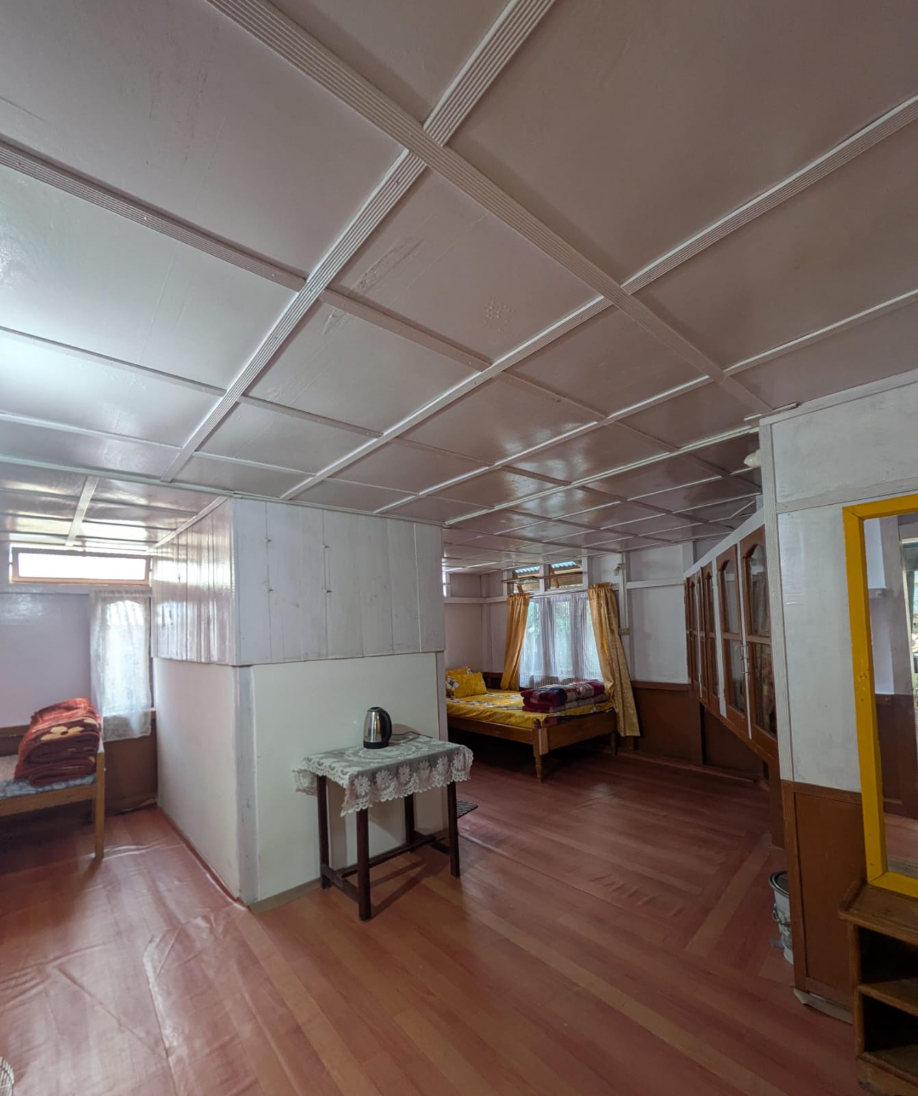 A wide room with a yellow double bed, a single bed in an alcove, and a small table with a kettle