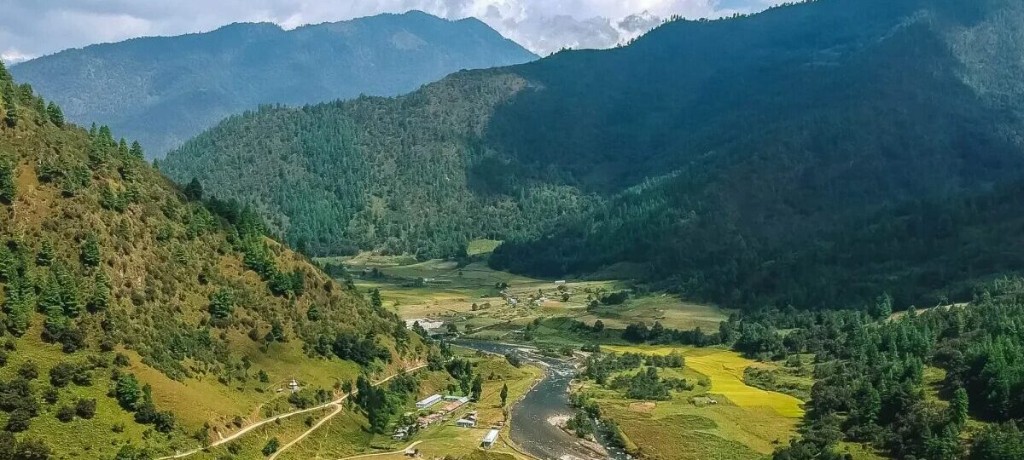 A river bending through rice fields, with forested ridges closing the valley
